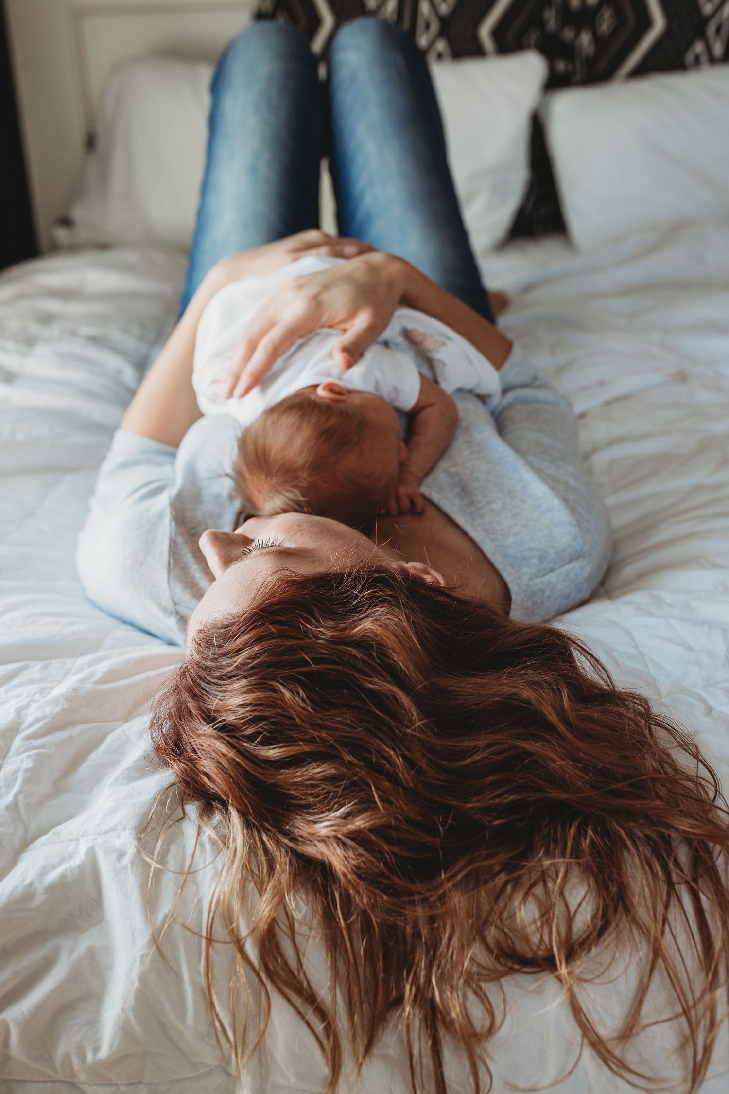 Mother holds baby girl to her chest and lays on bed with her hair spread out