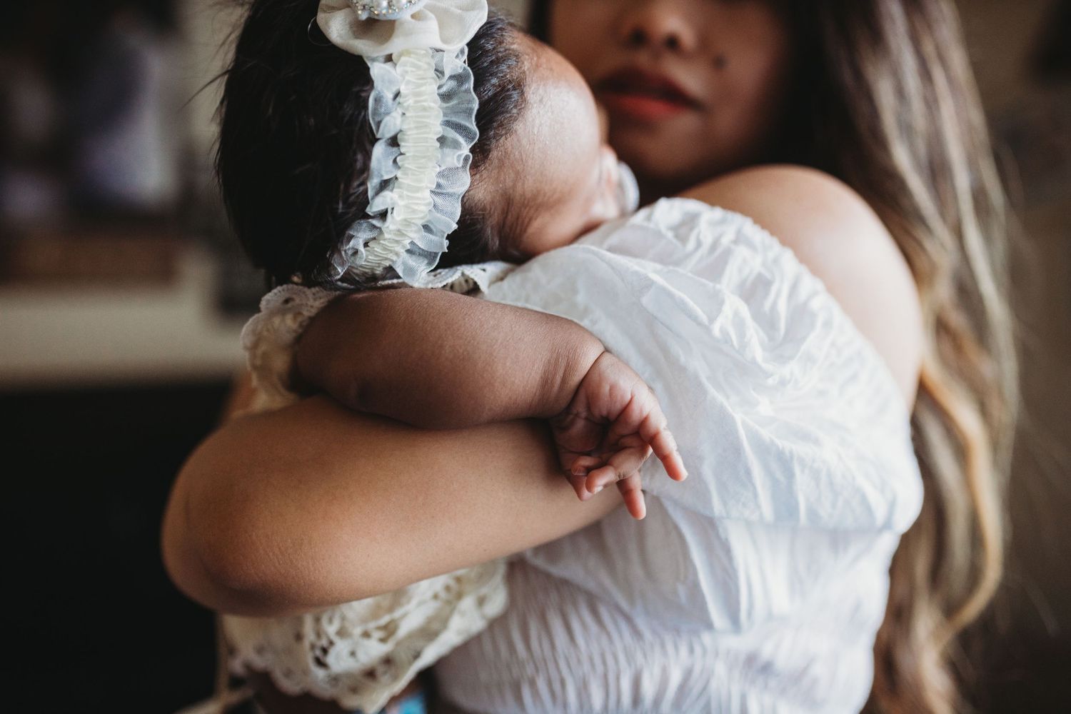 Close-up shot of a baby in white lace clothing being held against a white dress.