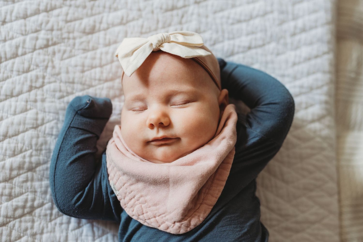 Sleeping baby girl with bow and bandana lays on a white quilt