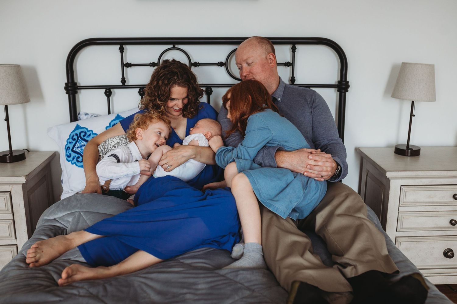 Family lounging together on a bed with matching blue outfits and white decor.