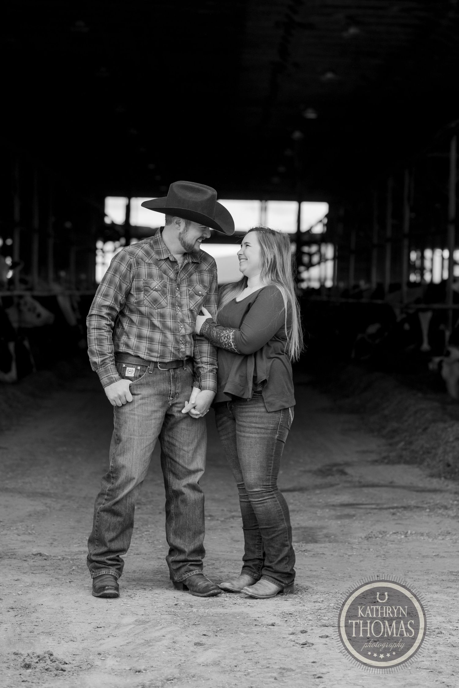 Black and white portrait of a western couple in a rustic barn setting.