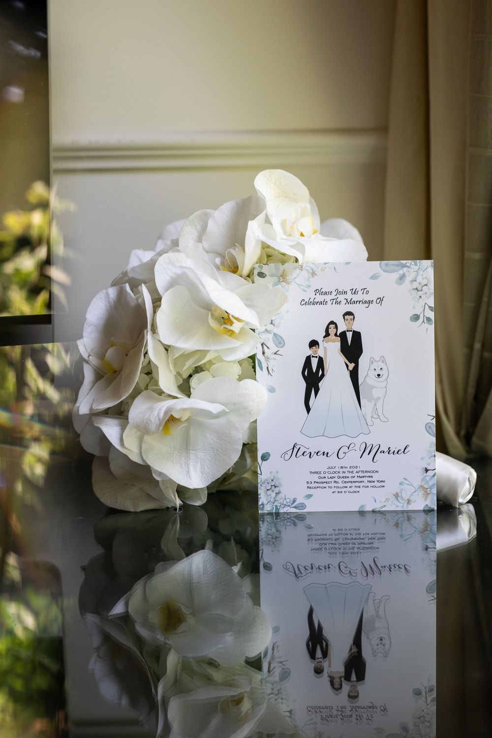 An elegant wedding invitation displayed with white orchids and subtle reflections.