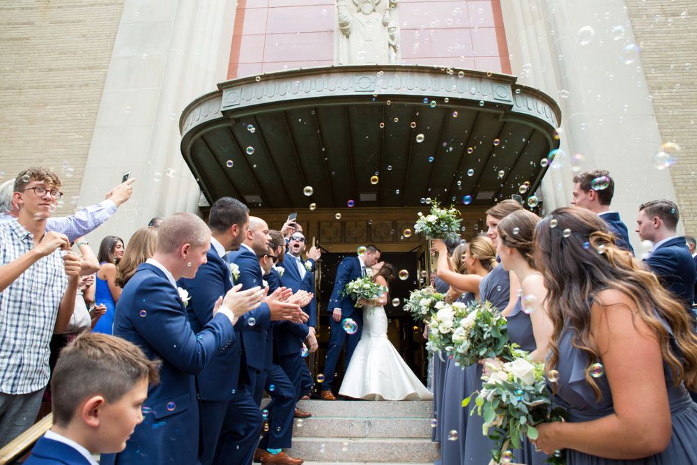 Wedding guests shower the newlyweds with flower petals as they exit a church on stone steps.