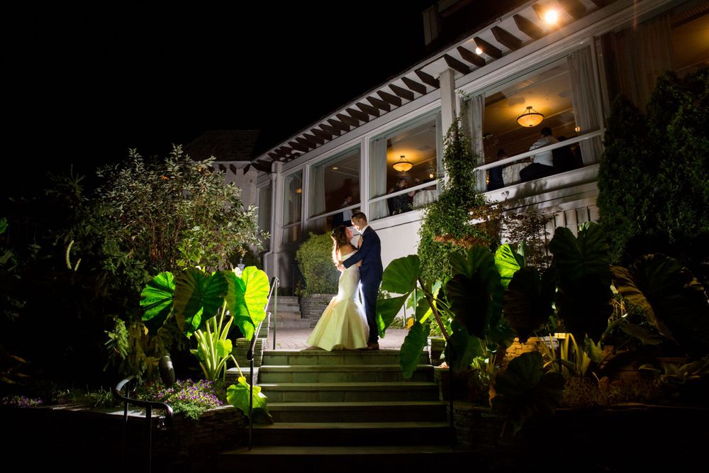 A dramatic nighttime wedding portrait on steps with illuminated landscaping.