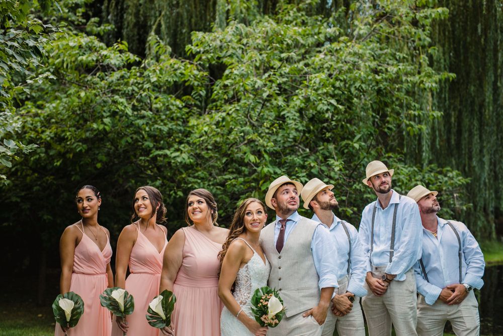Wedding party in pink and light blue attire poses together under weeping willow trees.