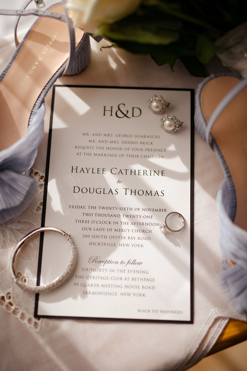 Wedding invitation with rings and delicate gray shoes arranged on lace fabric.