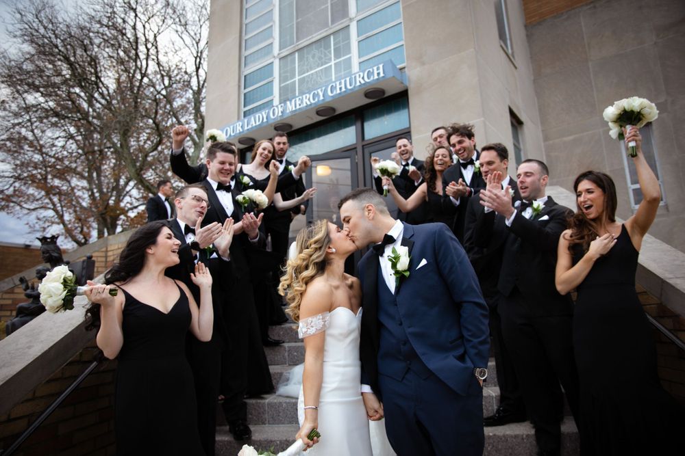 Wedding party in black attire poses dramatically on outdoor steps.