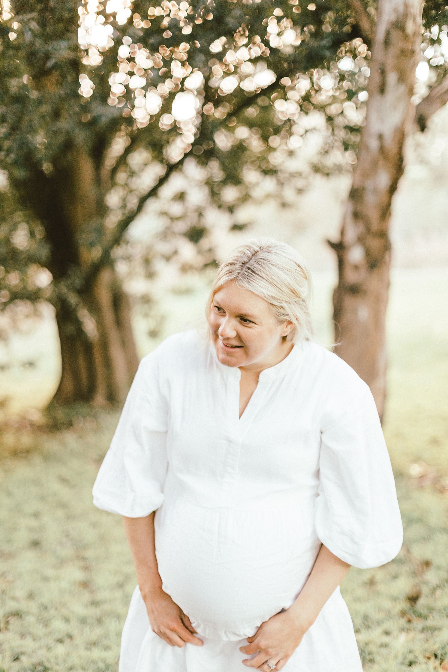 Woman in white dress sharing joyful moment outdoors under tree canopy.