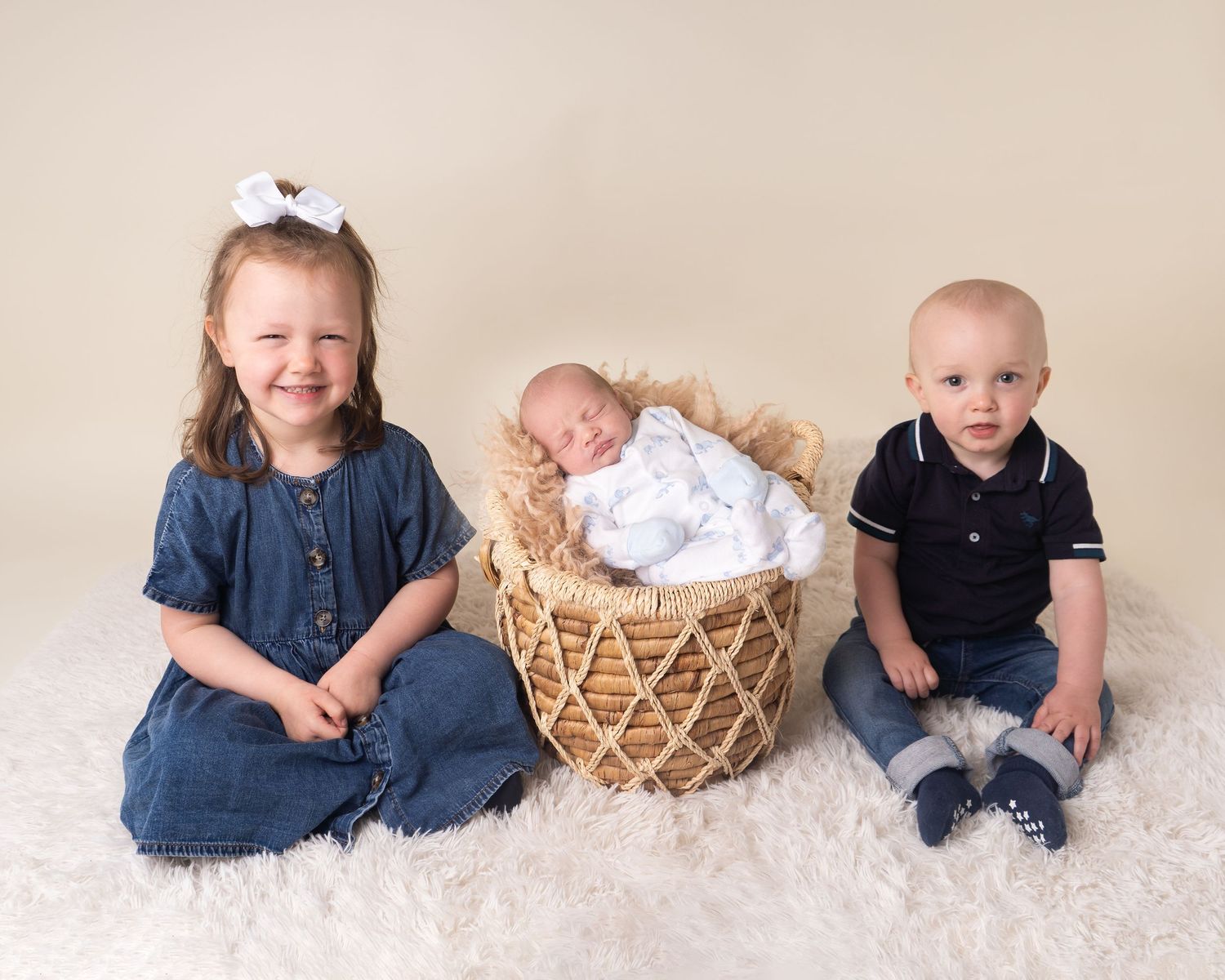 Newborn baby boy in a basket prop with siblings brother and sister sat on fluffy rug at newborn photoshoot in Doncaster.