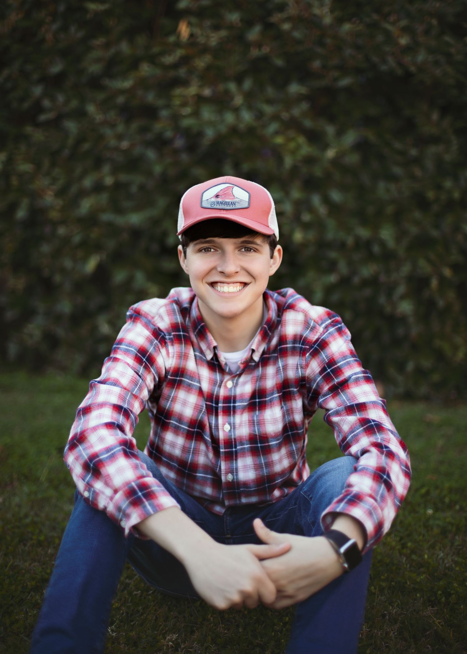Person in plaid shirt and baseball cap sitting casually outdoors.