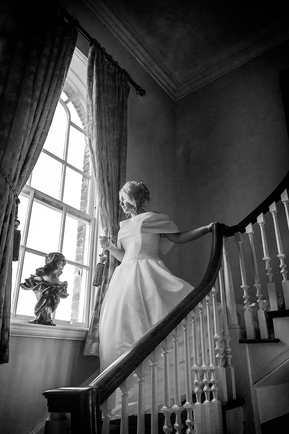 wedding photograph bride walking down stairs looking out of window with  doing in her hand at Stanbrook abbey