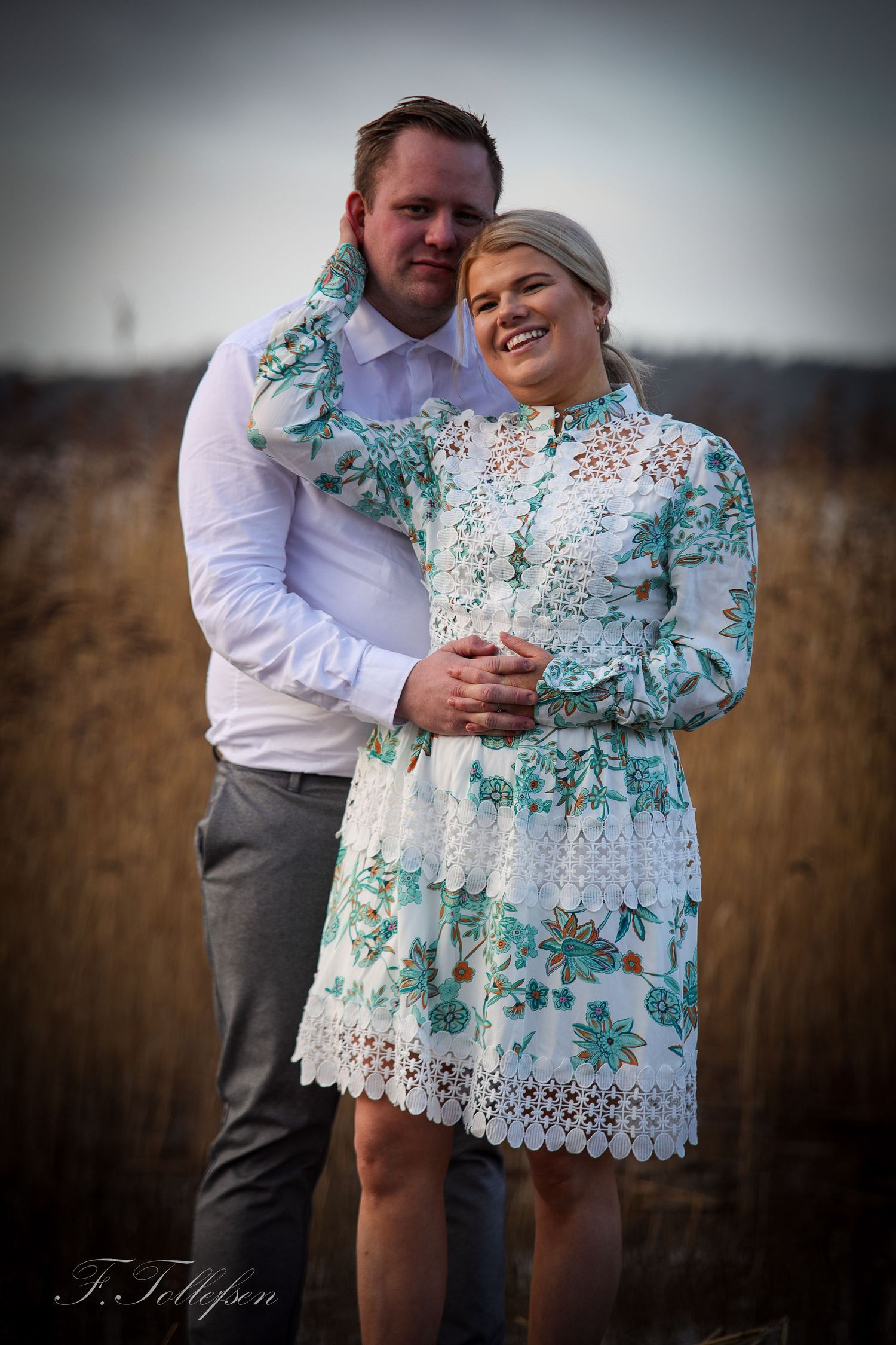 Happy couple posing together in a dry winter field, woman in a white floral lace dress.
