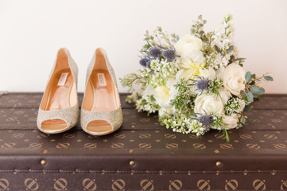 Bridal accessories including peach shoes and white floral bouquet arranged on wooden surface.