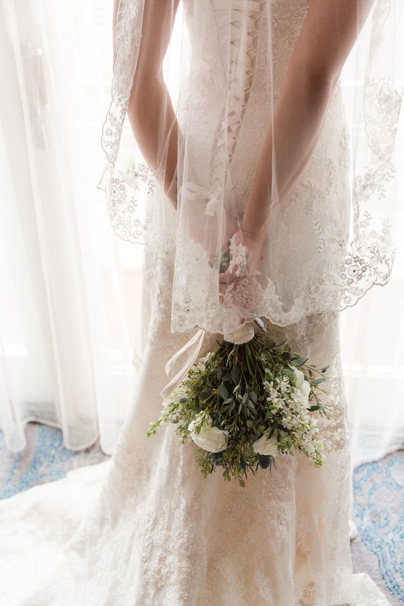 Close-up view of white lace wedding dress hem and bouquet details.