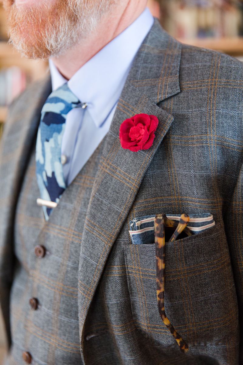 Close-up details of grey suit jacket with red boutonniere and navy tie.