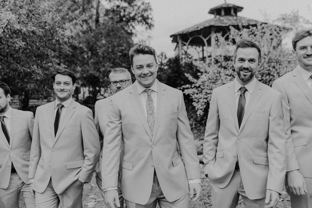 Black and white photo of groom and groomsmen in tan suits walking together outdoors.