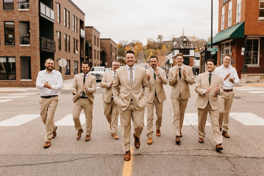 Groom and groomsmen in tan suits crossing a street in an urban setting on wedding day.