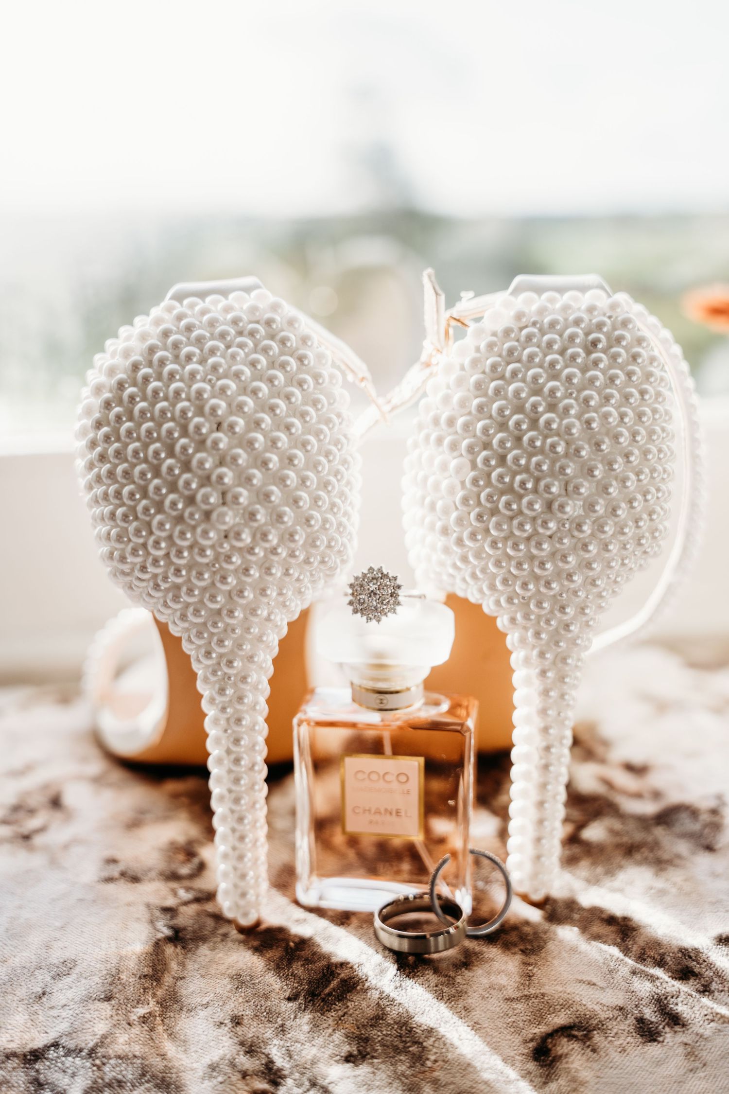 Pearl-embellished white bridal heels with perfume bottle and wedding rings.