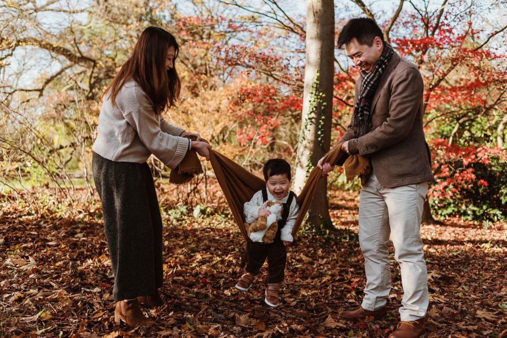 Family enjoying playful moments together in a park surrounded by fall foliage.