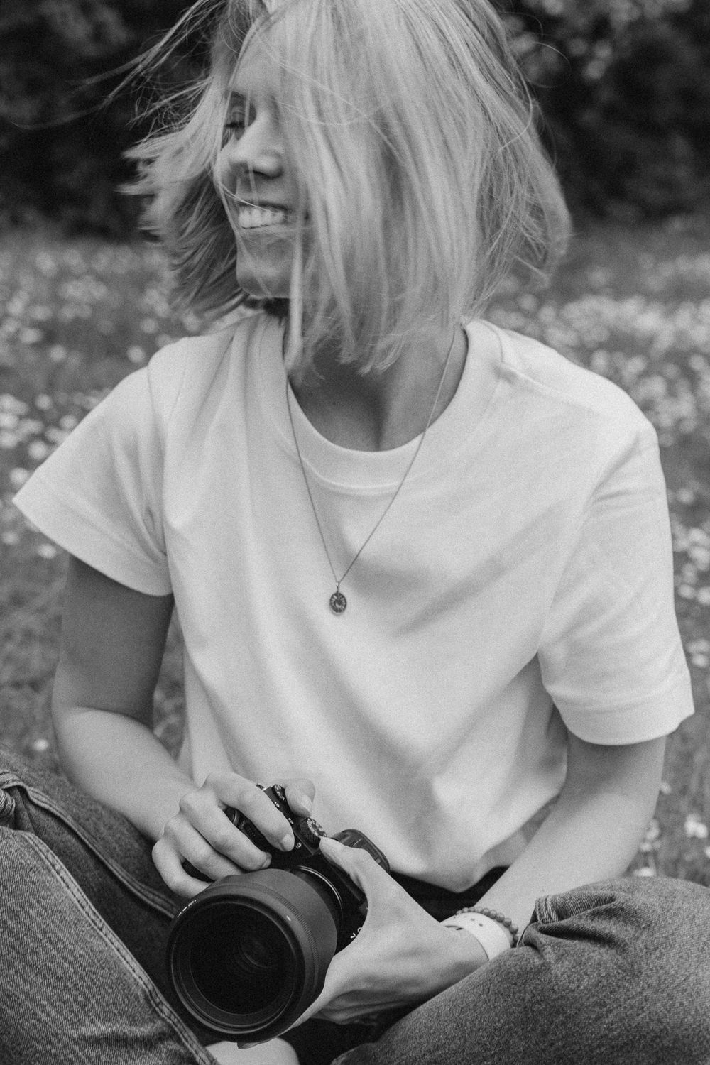 Candid black and white photo of someone laughing while holding a camera outdoors.