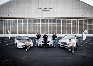 Luxury cars lined up in front of an industrial hangar building.