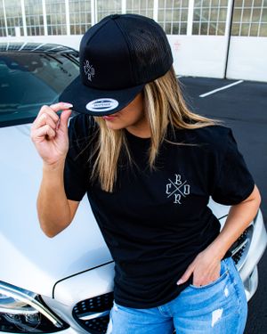 Person wearing black clothing posing with luxury cars.