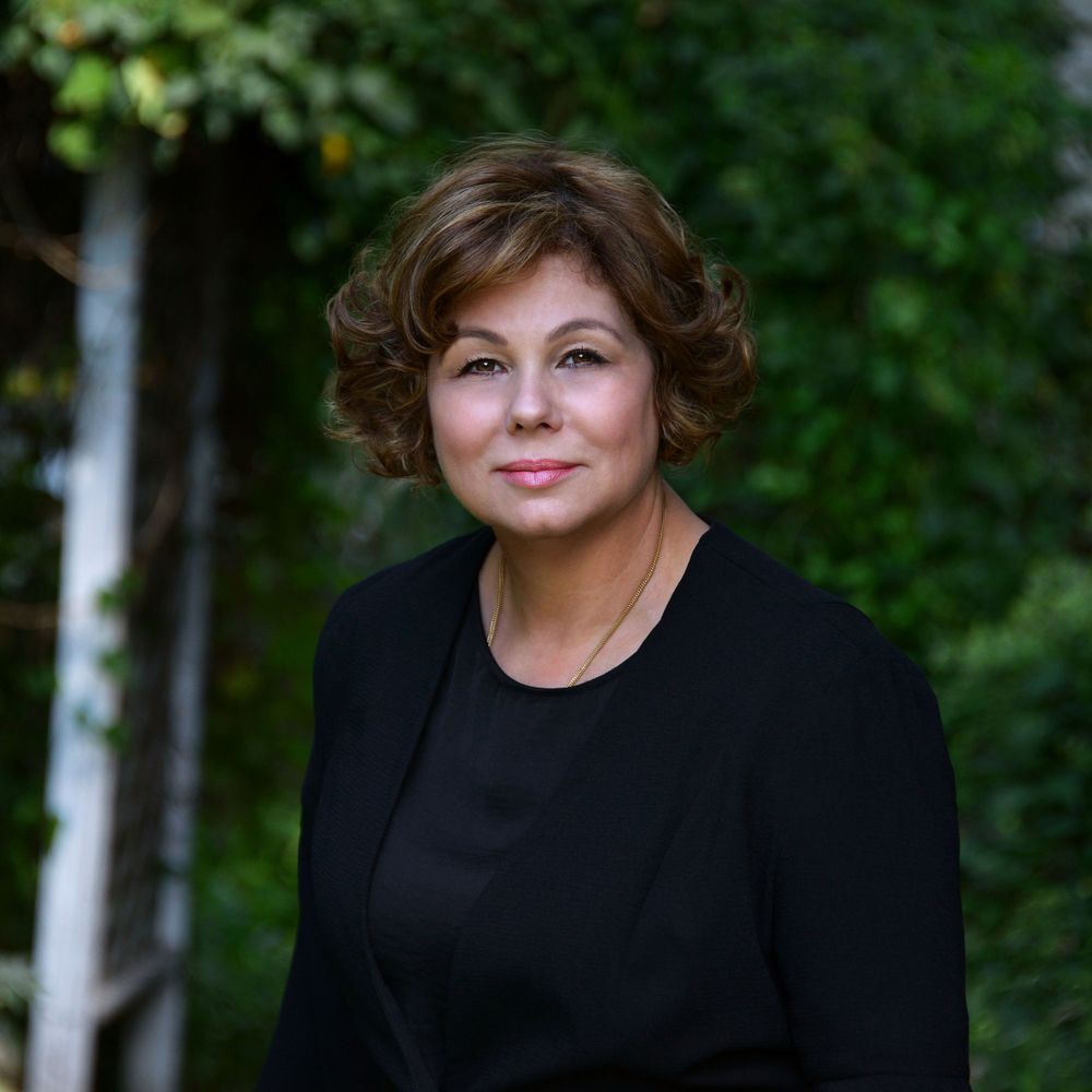Professional headshot of a person wearing a black blazer against a green background.