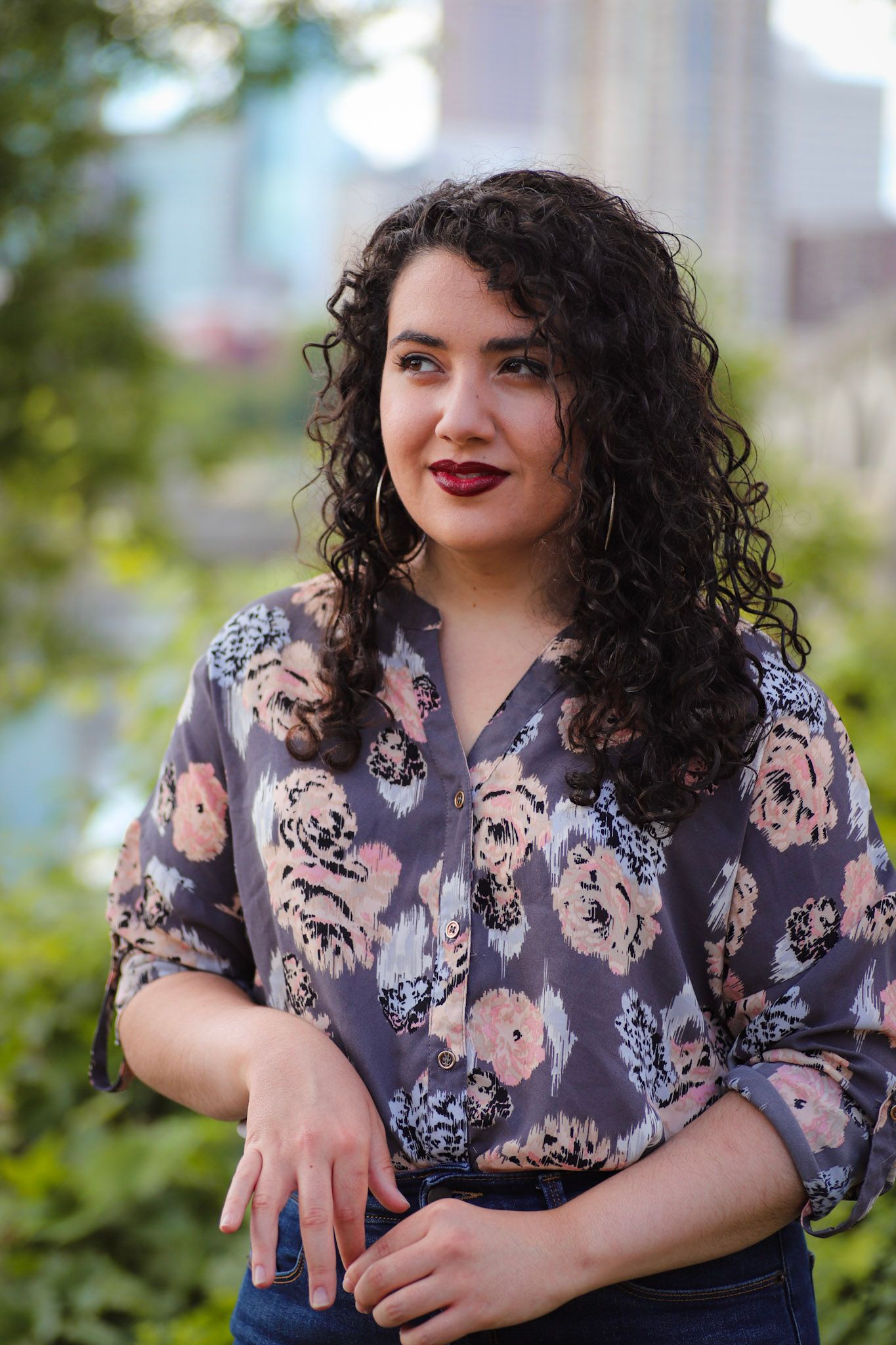 Professional portrait of a woman in a floral blouse with dark curly hair against an urban background.