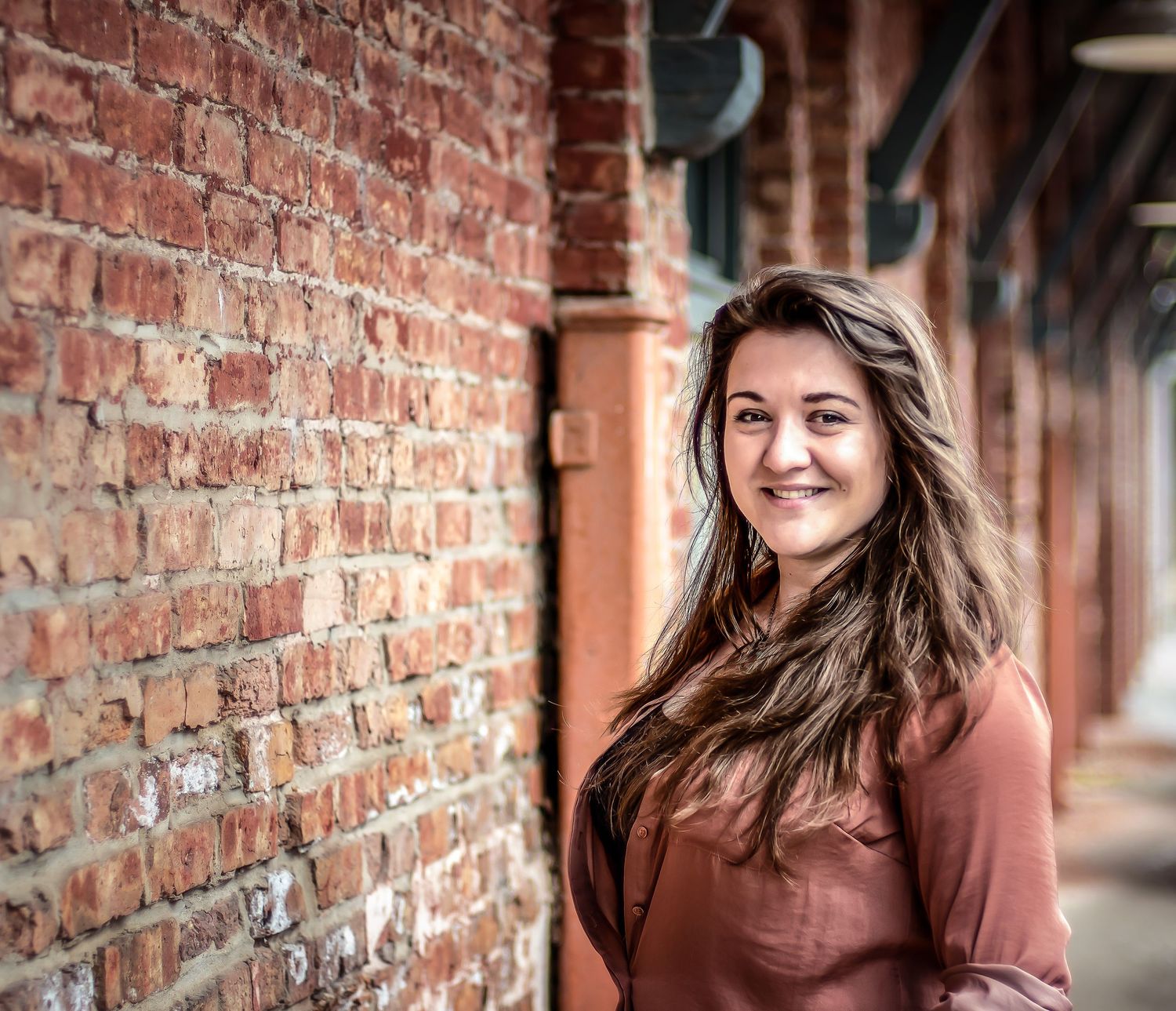 Portrait against rustic brick wall with warm lighting and shallow depth of field.