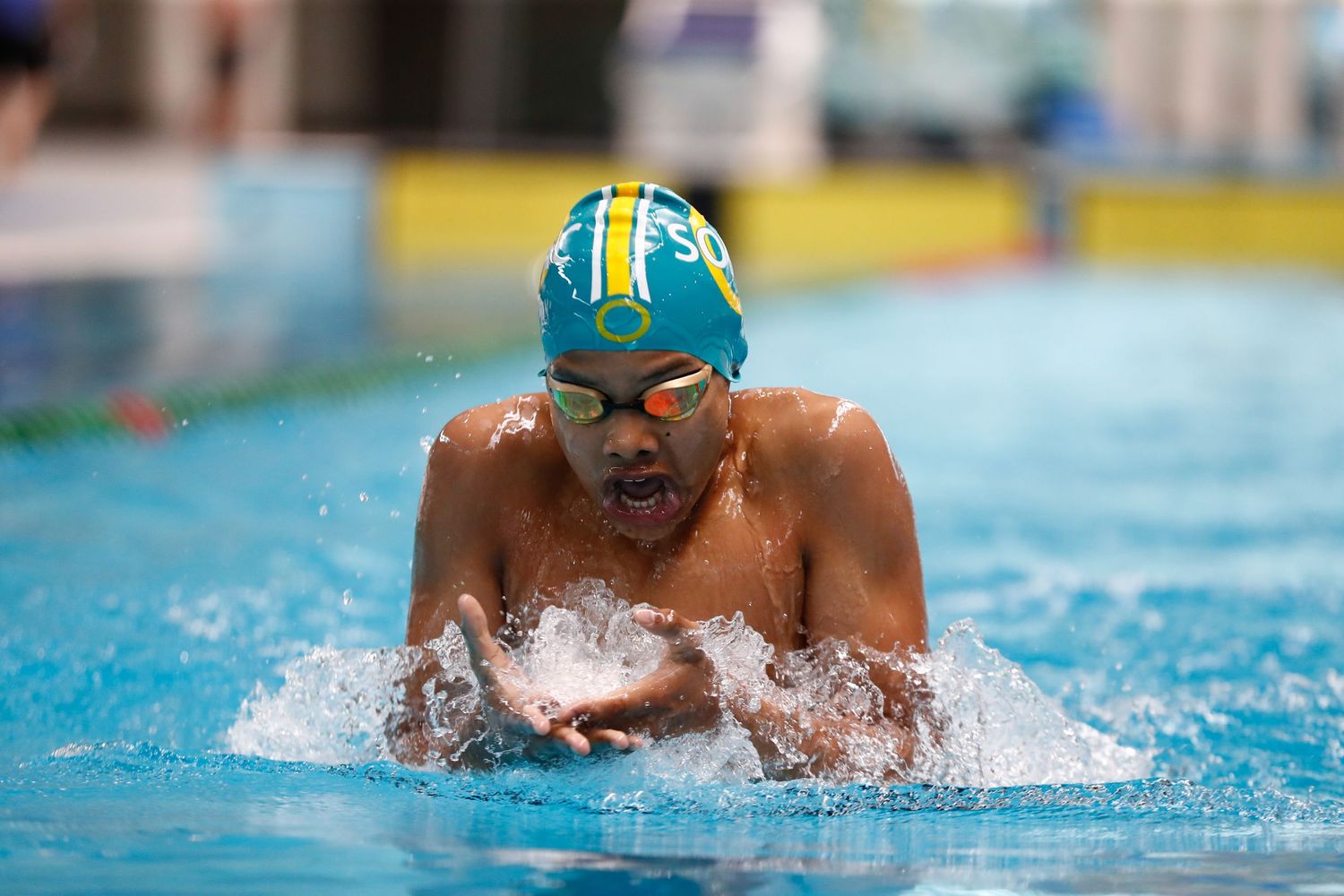 Swimmer performing breaststroke with water splashing in competition pool.