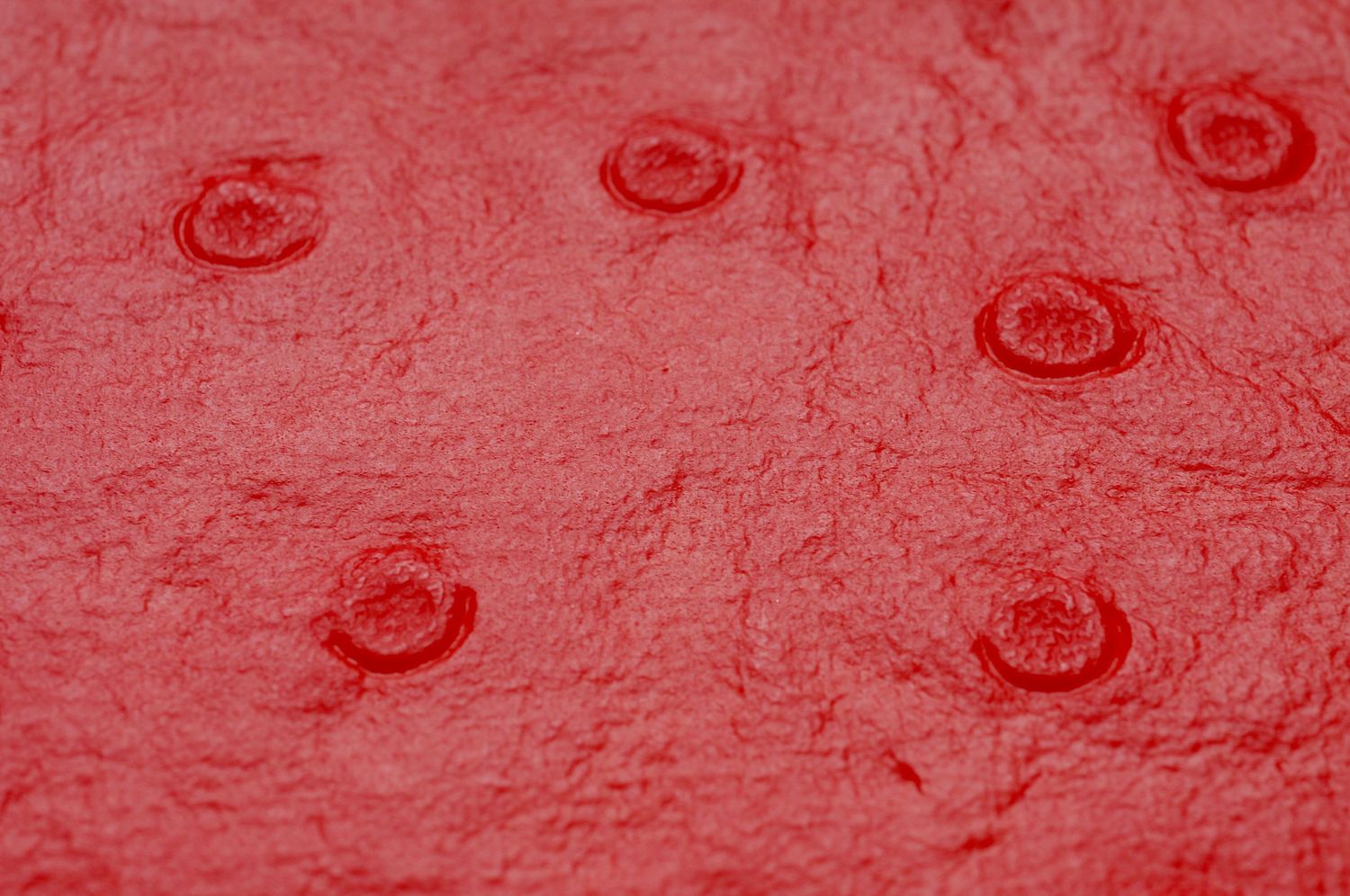Closeup view of water droplets creating circular ripples on a red textured surface.