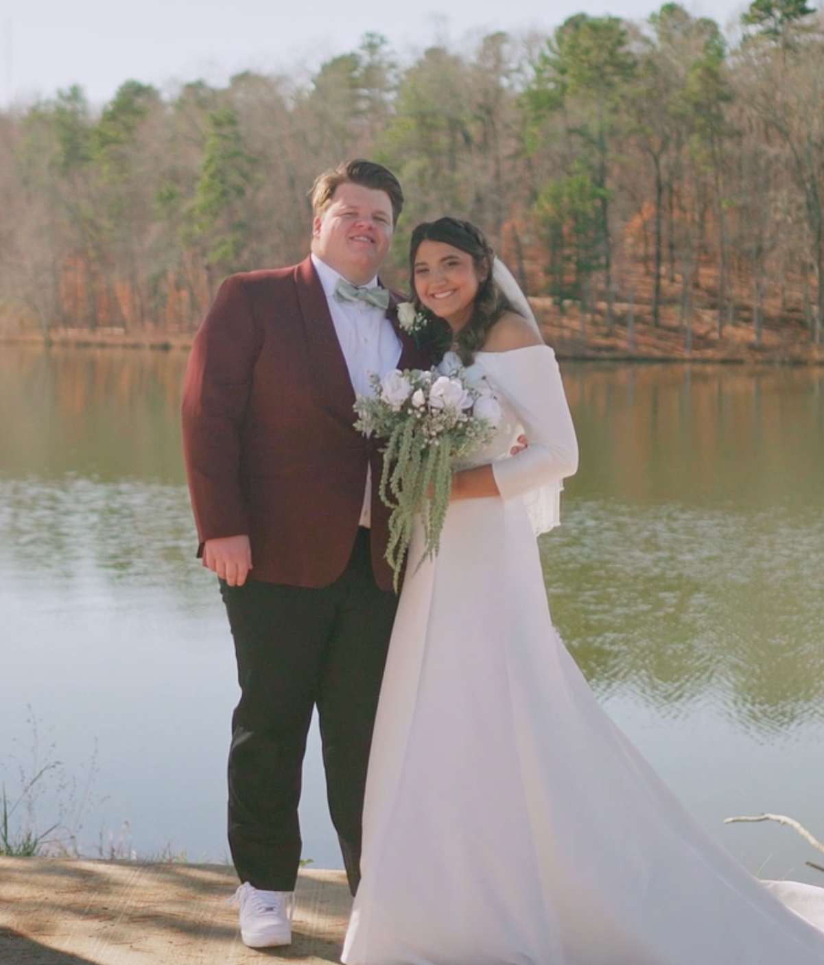 Couple standing in front of a lake with trees in the background