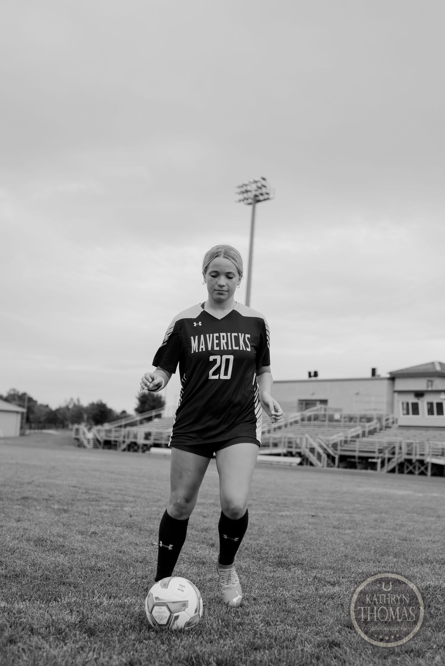 Black and white photo of soccer player in Mavericks uniform posing with ball on field.