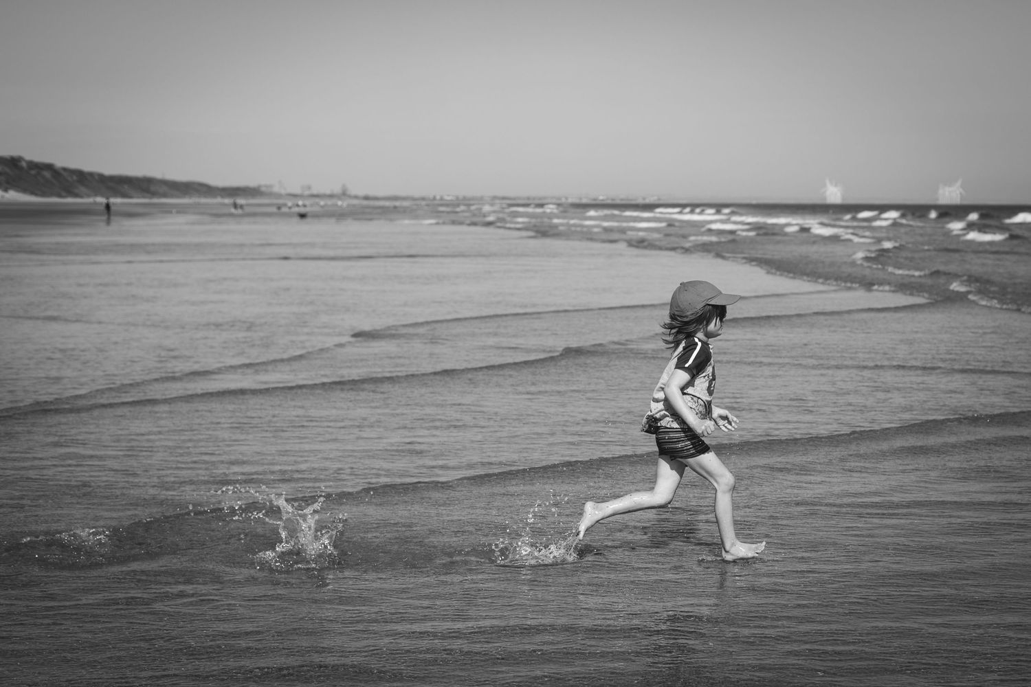 Black and white image of someone running and splashing through shallow beach water.
