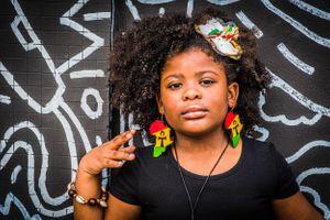 Creative portrait series against black wall with graffiti featuring bright green earrings and black attire.
