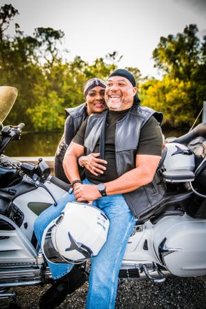 Romantic motorcycle photoshoot featuring a couple in casual attire sitting on parked bikes at sunset.