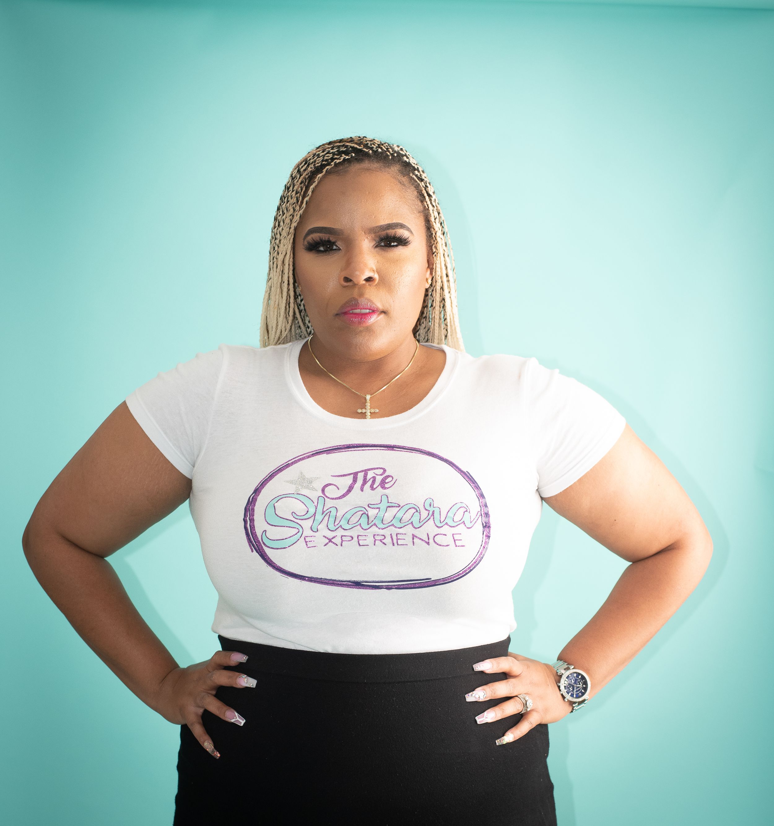 Casual brand photoshoot in white logo t-shirt and black pants against turquoise background.