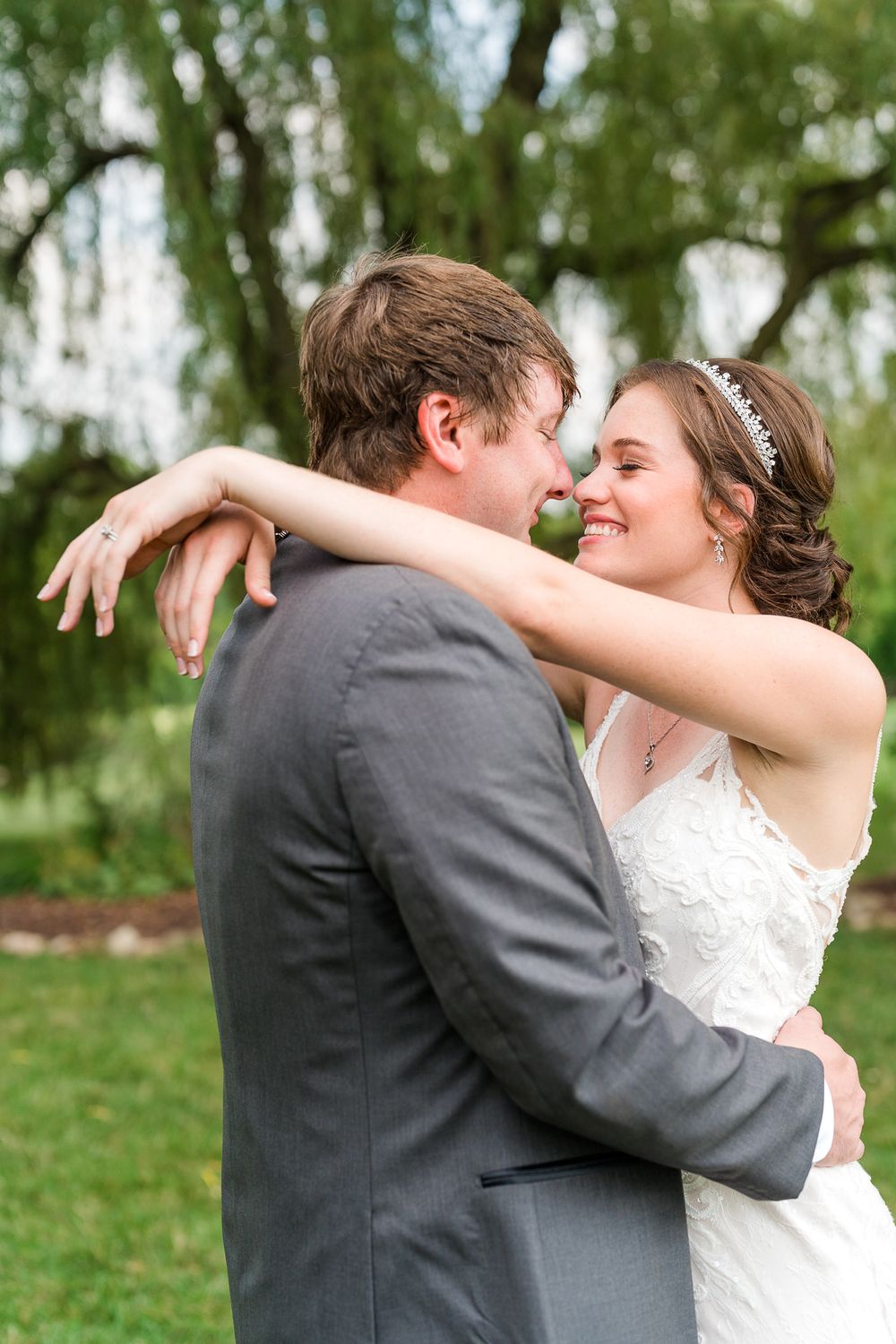 A romantic wedding couple embraces outdoors under a willow tree during their special day.