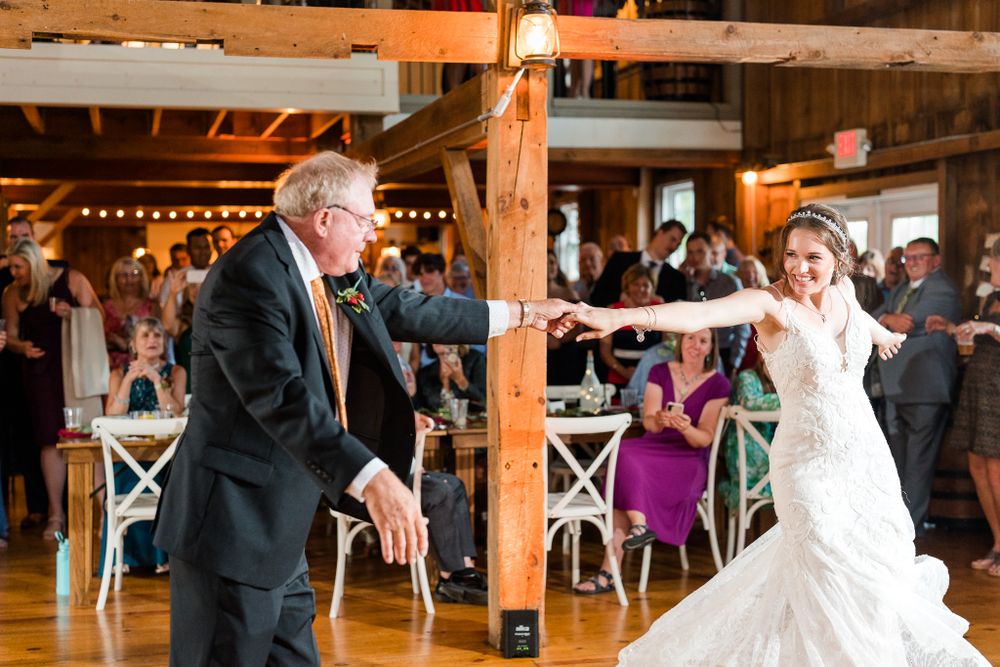 Wedding couple dances joyfully in a rustic barn venue with string lights and wooden beams.