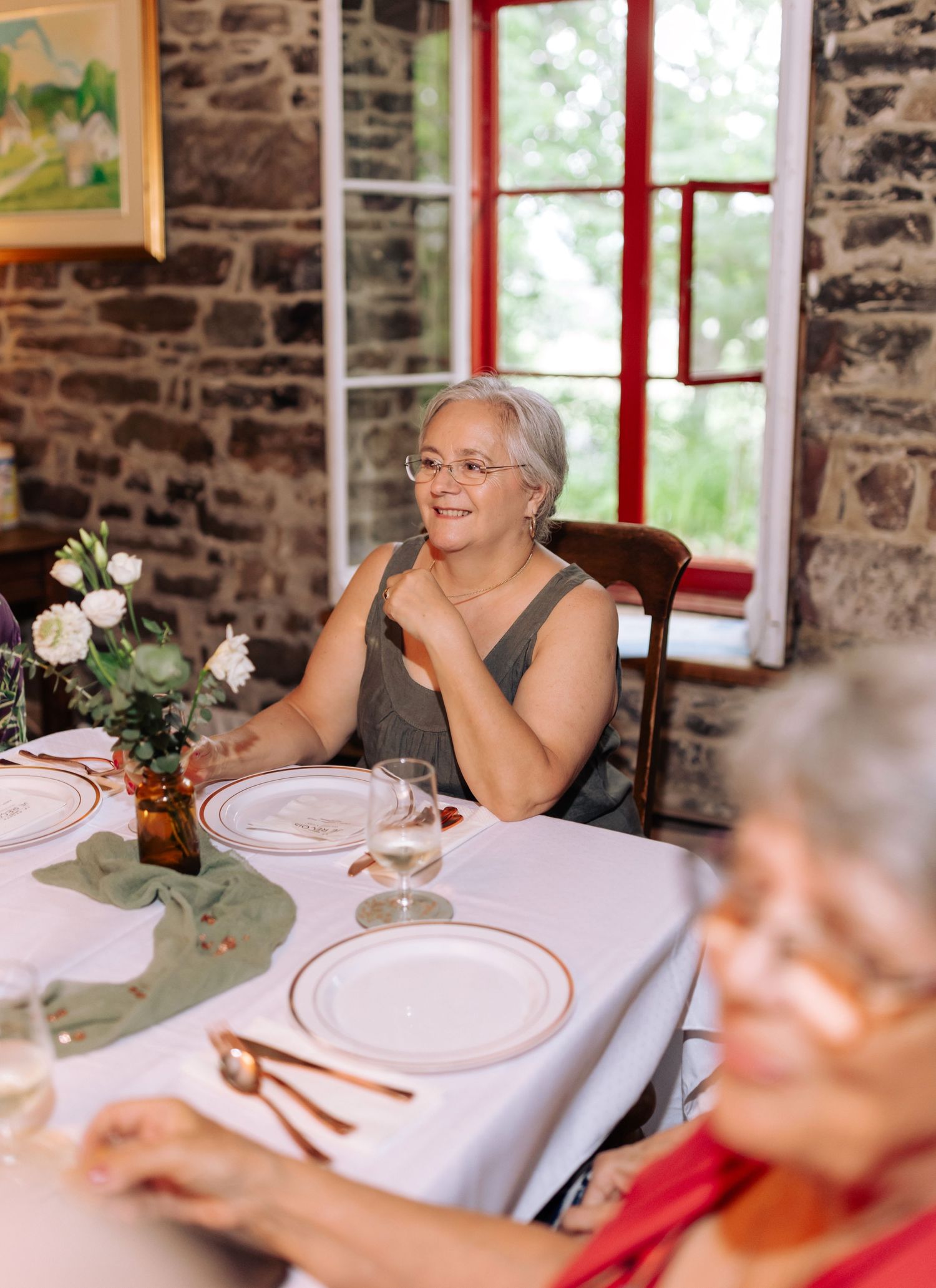 Elegant dinner party in a rustic stone building with white table settings and floral decorations.