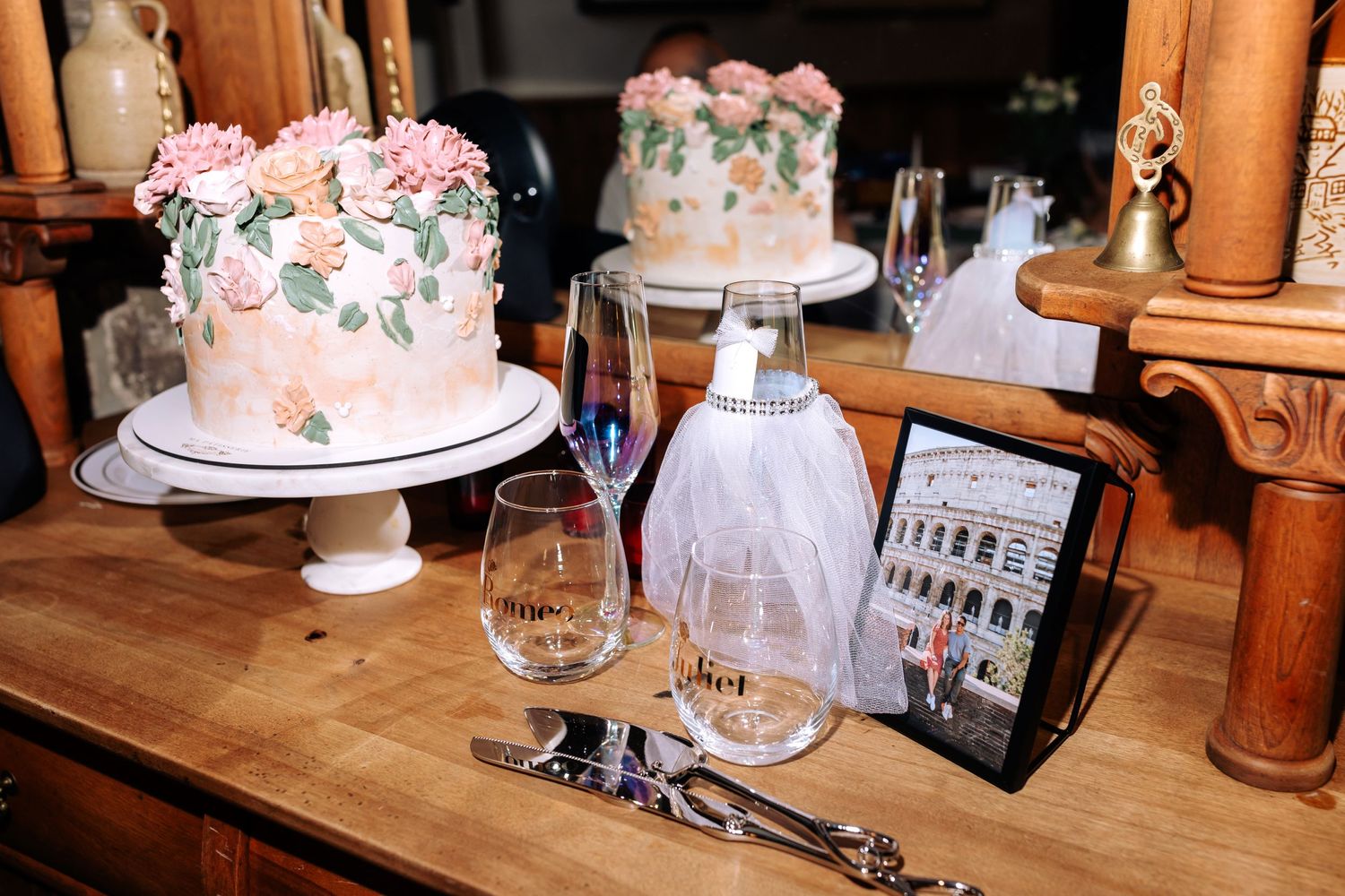 Beautiful pink floral wedding cake and table settings with wine glasses in a rustic venue.