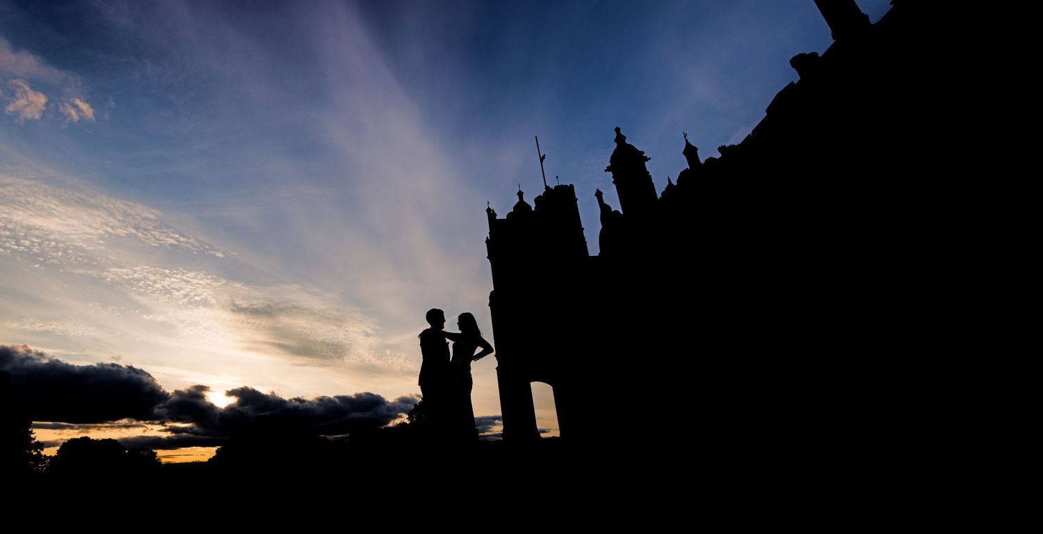 Silhouetted couple against a dramatic sunset sky with gothic architecture in background.