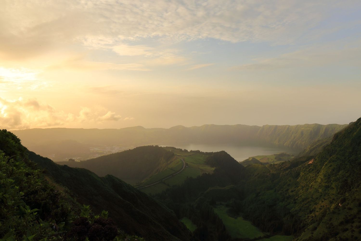 Sweeping vista of green volcanic valleys and lakes under a misty sunset sky.
