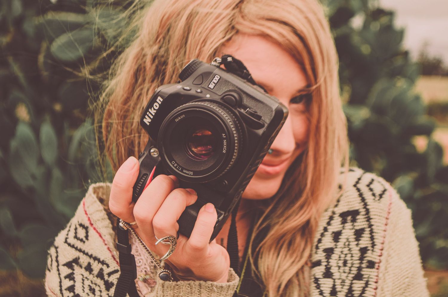 Photographer with a vintage camera wearing a cozy knit sweater in natural outdoor lighting.