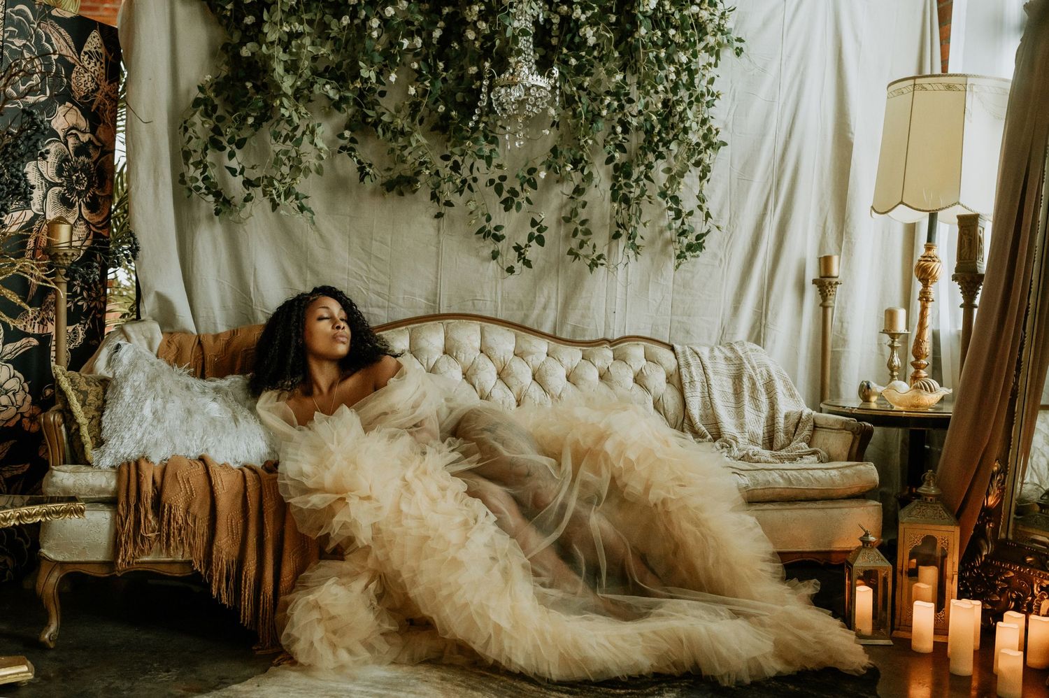 Romantic boudoir photo featuring flowing tulle dress on vintage chaise lounge with candles and greenery.
