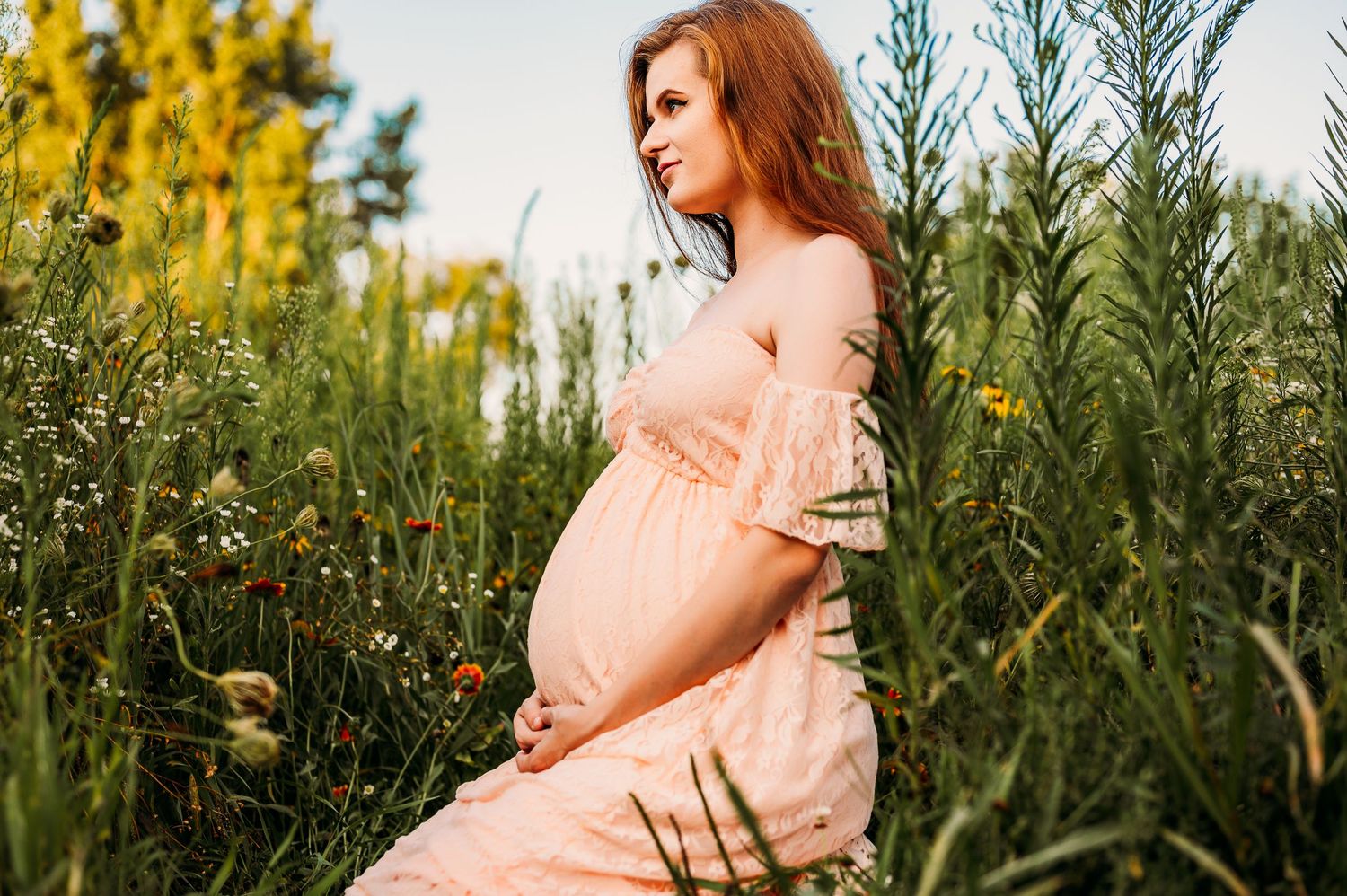 Pregnant woman wearing pink holding belly in a field of flowers in Staten Island