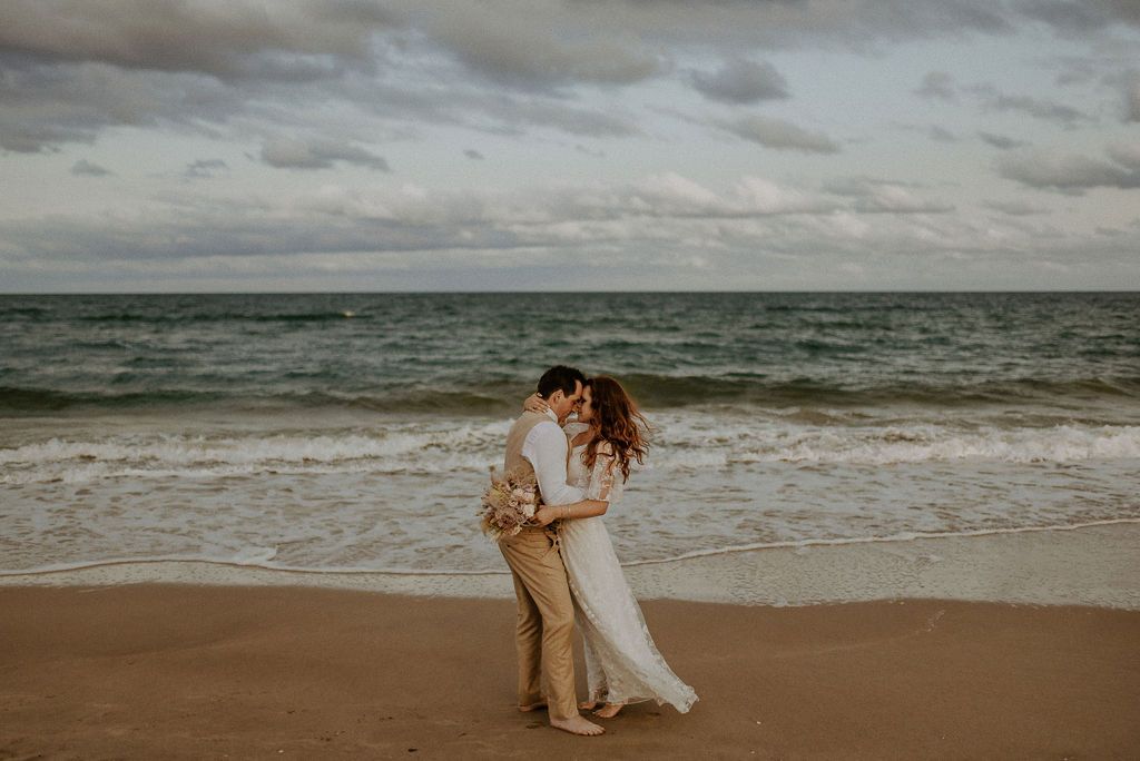 Couple walking along a cloudy beach with waves crashing on the shore.