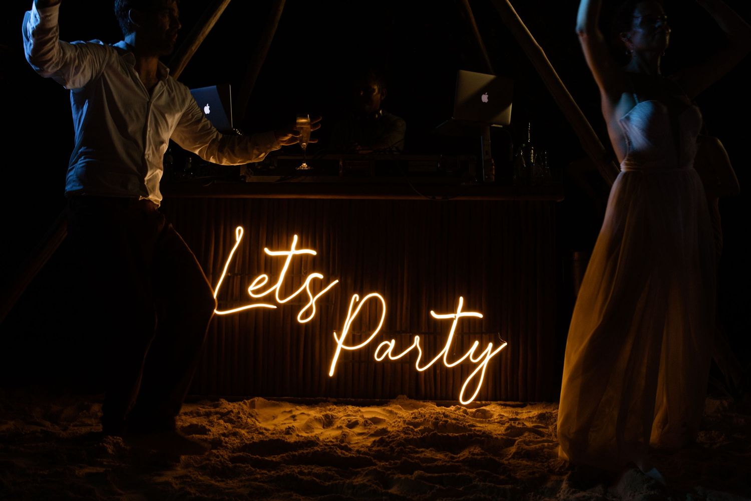 Illuminated 'Let's Party' neon sign glowing against a dark background at a nighttime celebration. Wedding photographer in Mexico Riviera May