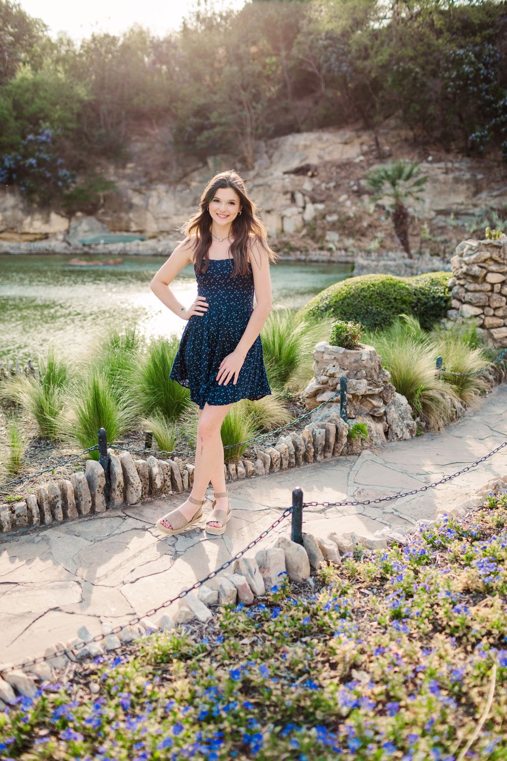 Woman in navy dress standing among blooming flowers on stone pathway.