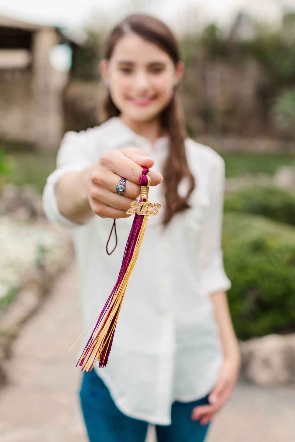 Hand holding graduation tassel with ring detail against garden background.